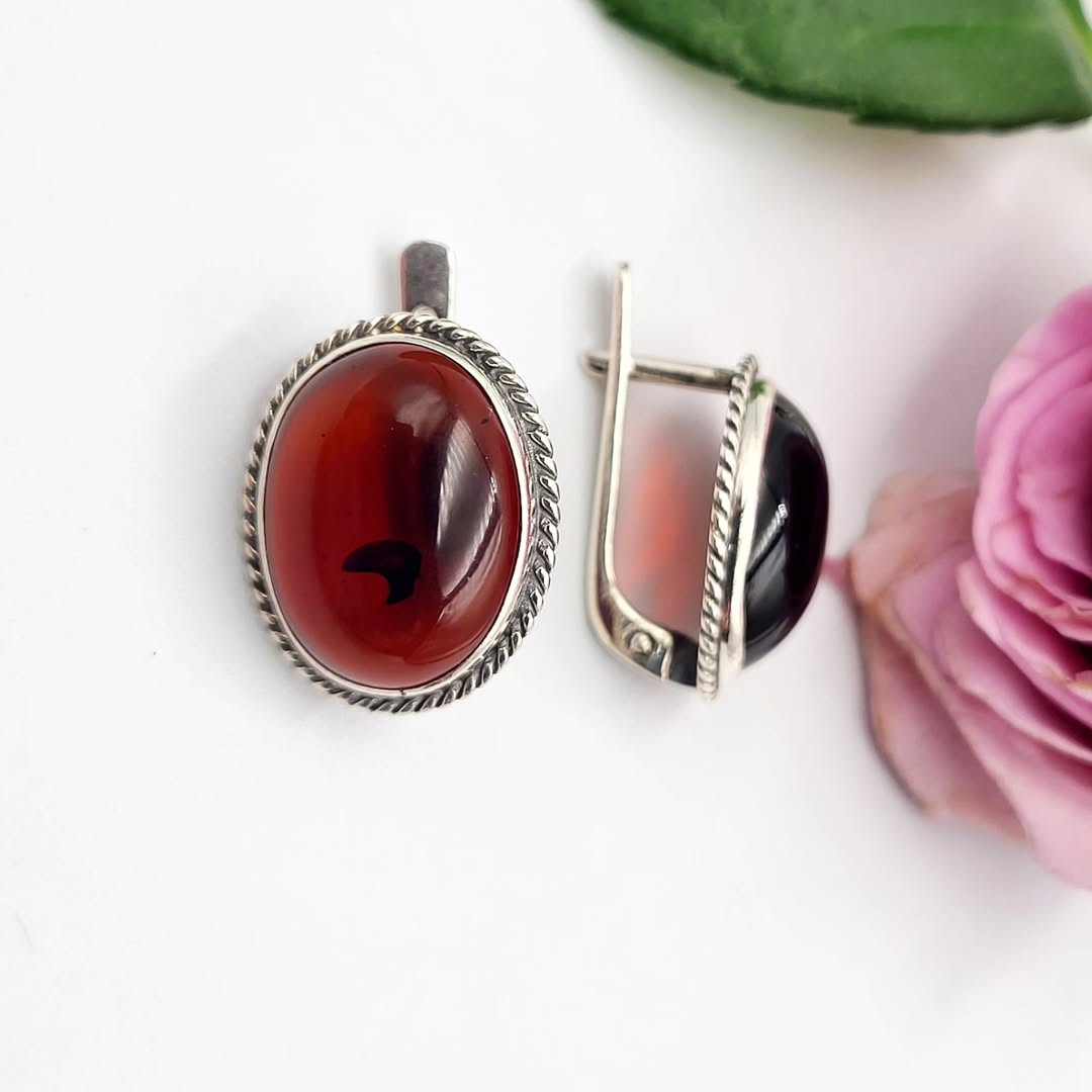 Two silver earrings with red and black stones on a white background with a pink flower.