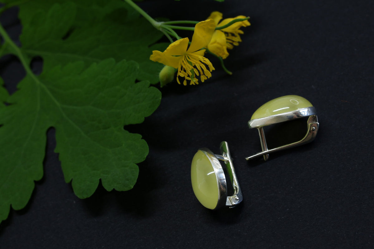 Green earrings on a dark background with yellow flowers and green leaves.