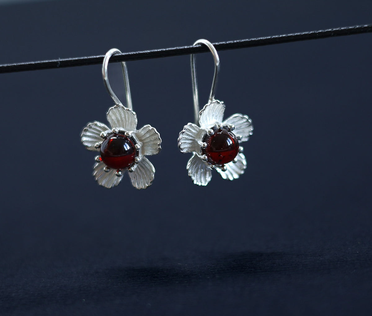 Ohrringe im Antik-Stil mit Silberblume und Kirschbernstein, präsentiert mit dem Ohrhaken vor hellem Hintergrund.