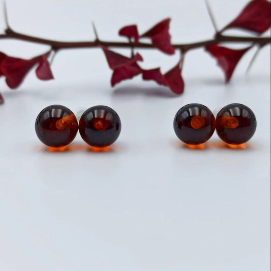 Kirschroter Bernstein Ohrstecker mit 925 Sterling Silber Stiften. Ansicht betont die glänzenden, runden Cognac Bernstein Kugeln.