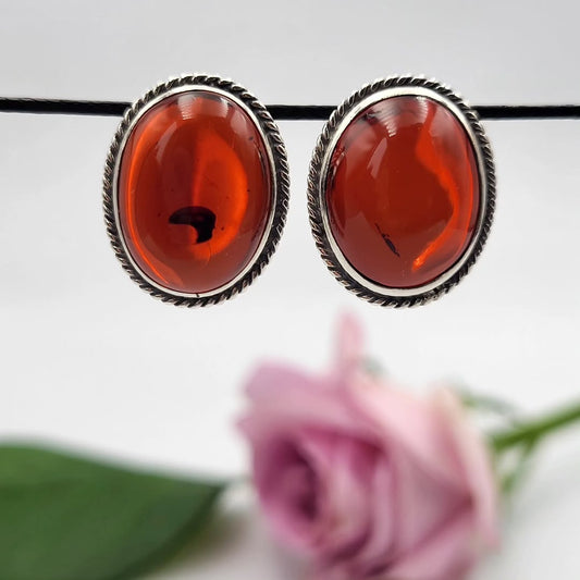 Ein dunkelroter Bernstein-Ohrring auf einem hellgrauen Stein, umrahmt von Heidekraut und Moos.