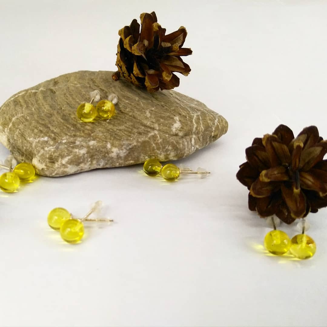 Sortiment der Lemon-Grün Bernstein Ohrringe (7mm, 8mm, 9mm), präsentiert auf einem Stein und zwischen Pinienzapfen.