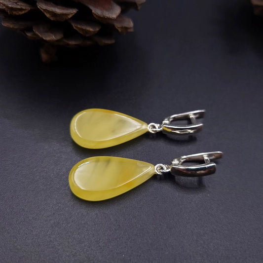 Pair of yellow teardrop earrings with silver hooks on a dark surface. Tropfen-Ohrhänger
