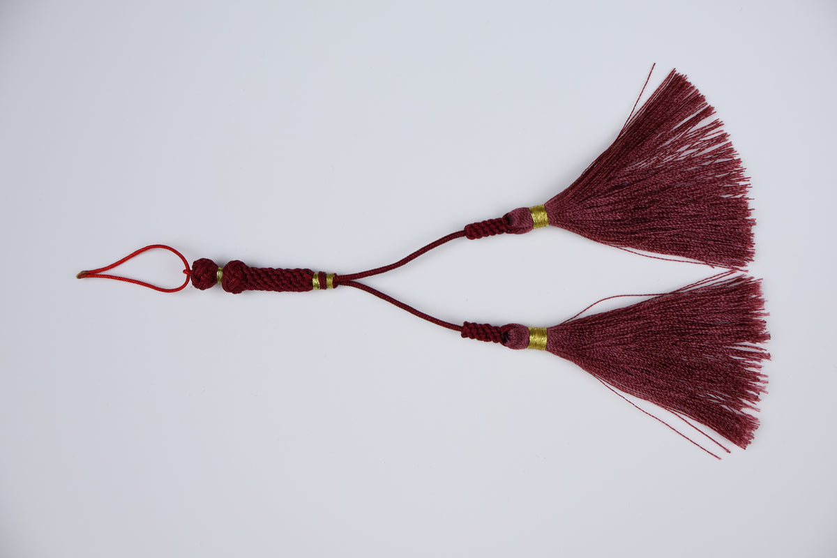 A pair of traditional arabic tassel ornaments in deep burgundy red, featuring braided cords, small gold spacer beads, and a hanging loop, displayed on a clean white background.