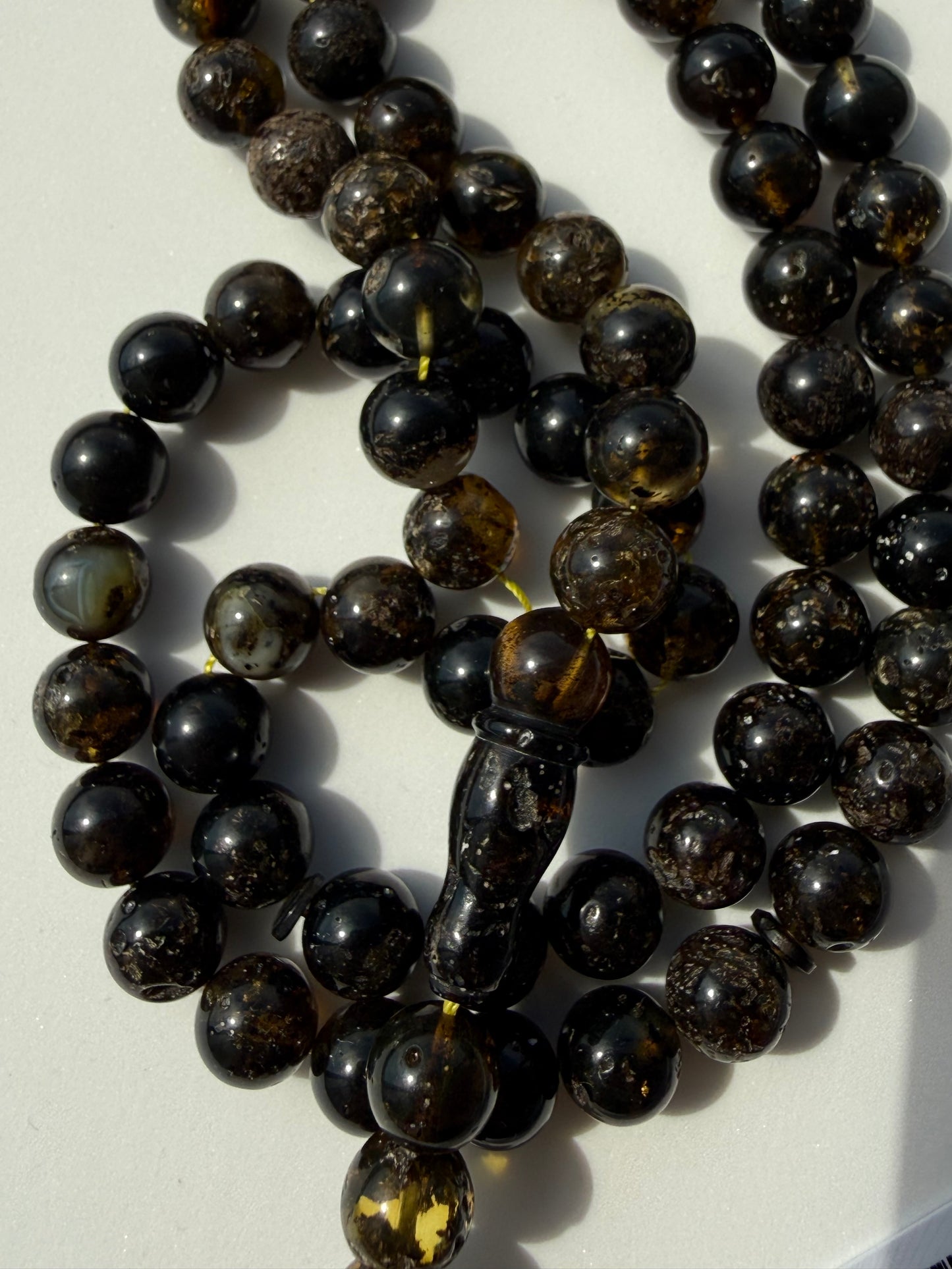 A strand of dark brown and black polished amber beads with natural inclusions, arranged on a light off-white background.
