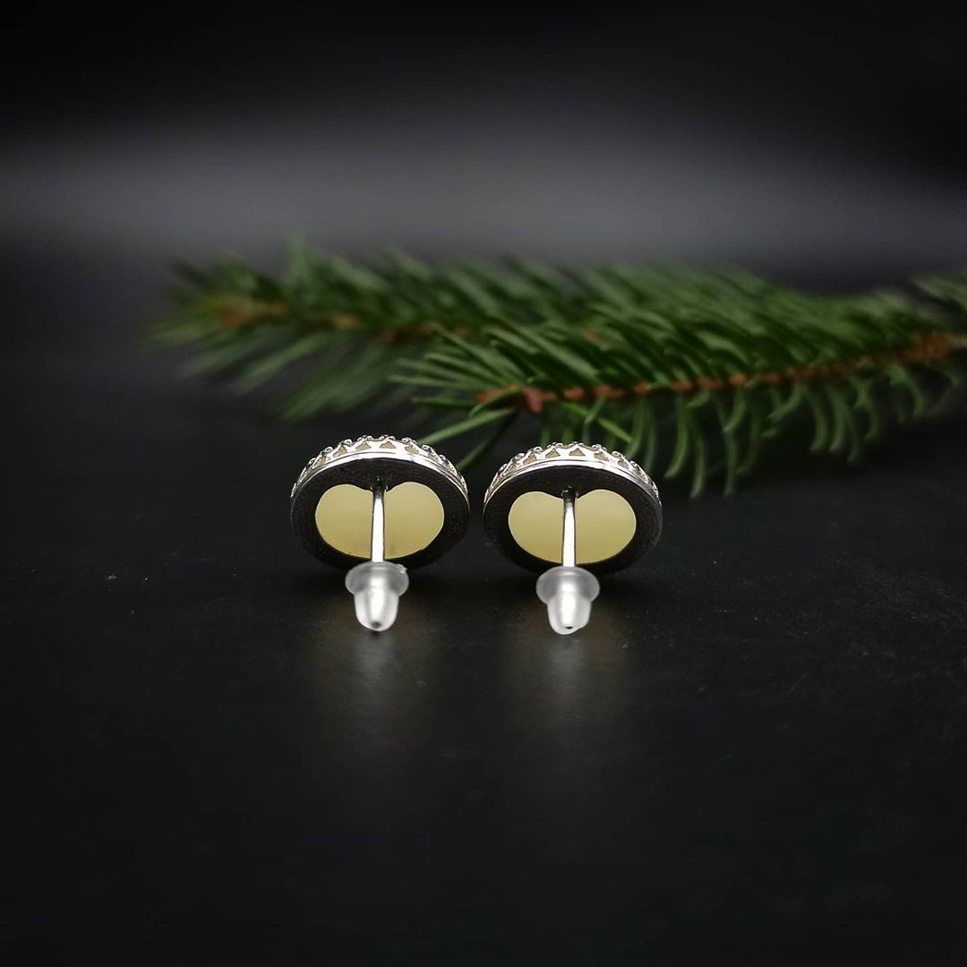 Rückansicht eines Tetibel Jewels Butterscotch Baltische Bernstein Ohrsteckers (⌀12mm) in 925 Sterling Silber mit sichtbarem Stift und Silikonverschluss. Ein weiterer Ohrstecker liegt im Vordergrund.