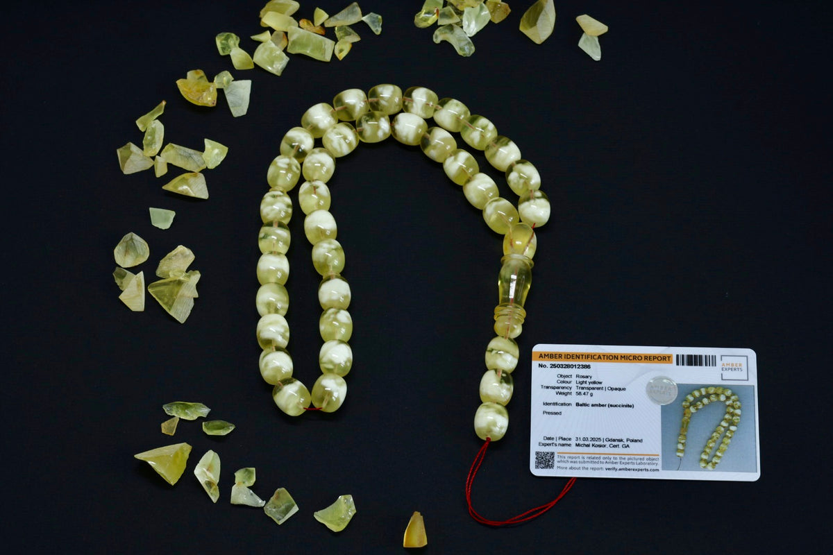 A string of light yellow amber prayer beads laid out on a black surface, with some beads detached from the string, and an authentication card included.