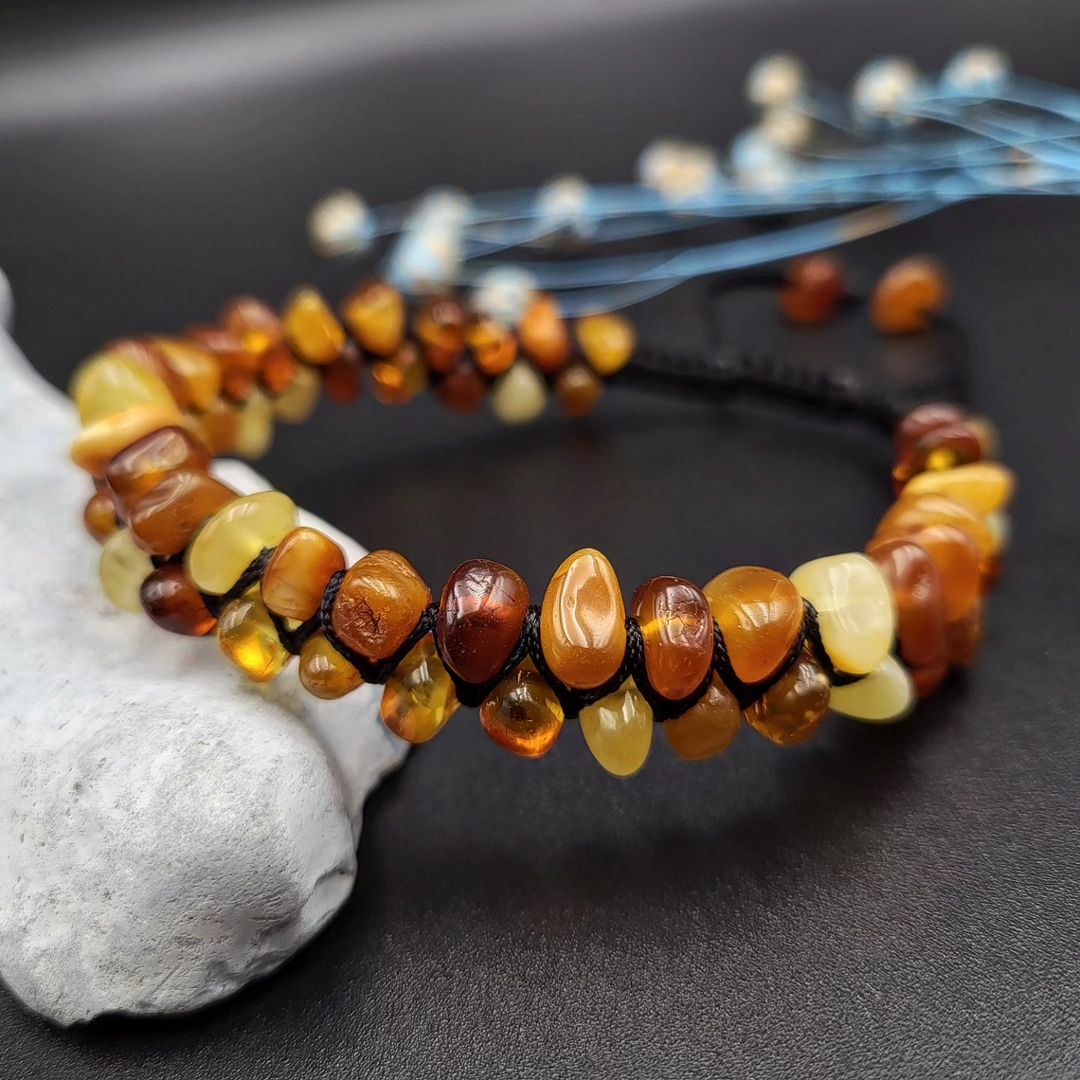 A woven amber bracelet featuring various shades of amber beads, displayed on a dark surface.
