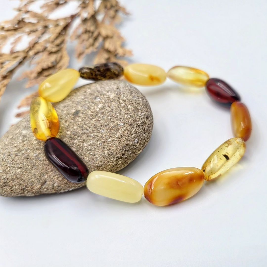 Tetibel Multi-Color Baltic Amber Bracelet featuring polished olive-shaped beads in lemon, honey, and cognac hues on a white background.
