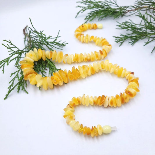 Nahaufnahme der Tetibel Rohbernstein-Splitterkette in Butterscotch und Lemon, spiralförmig auf weißem Hintergrund. Der Fokus liegt auf den unpolierten Nuggets und dem Kunststoff-Schraubverschluss.