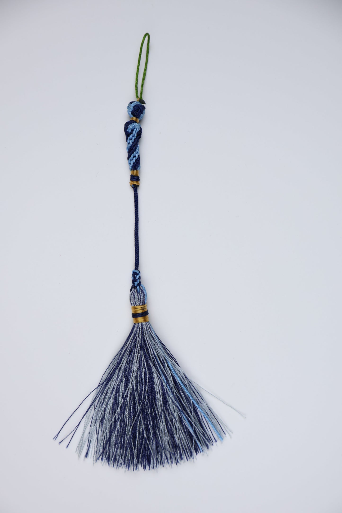 A traditional Islam tassel featuring a dark blue wrapped handle, a green loop for a cord, and a fan-shaped tassel made of blue, navy, and white silk threads, shown on a plain white background.
