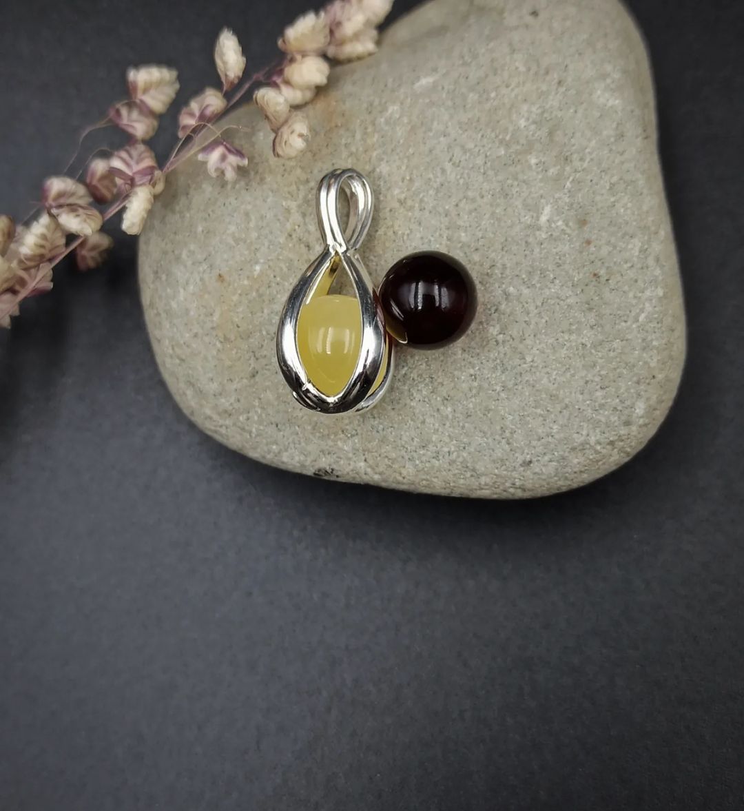 Silver pendant with yellow and brown changeable amber beads on a stone surface