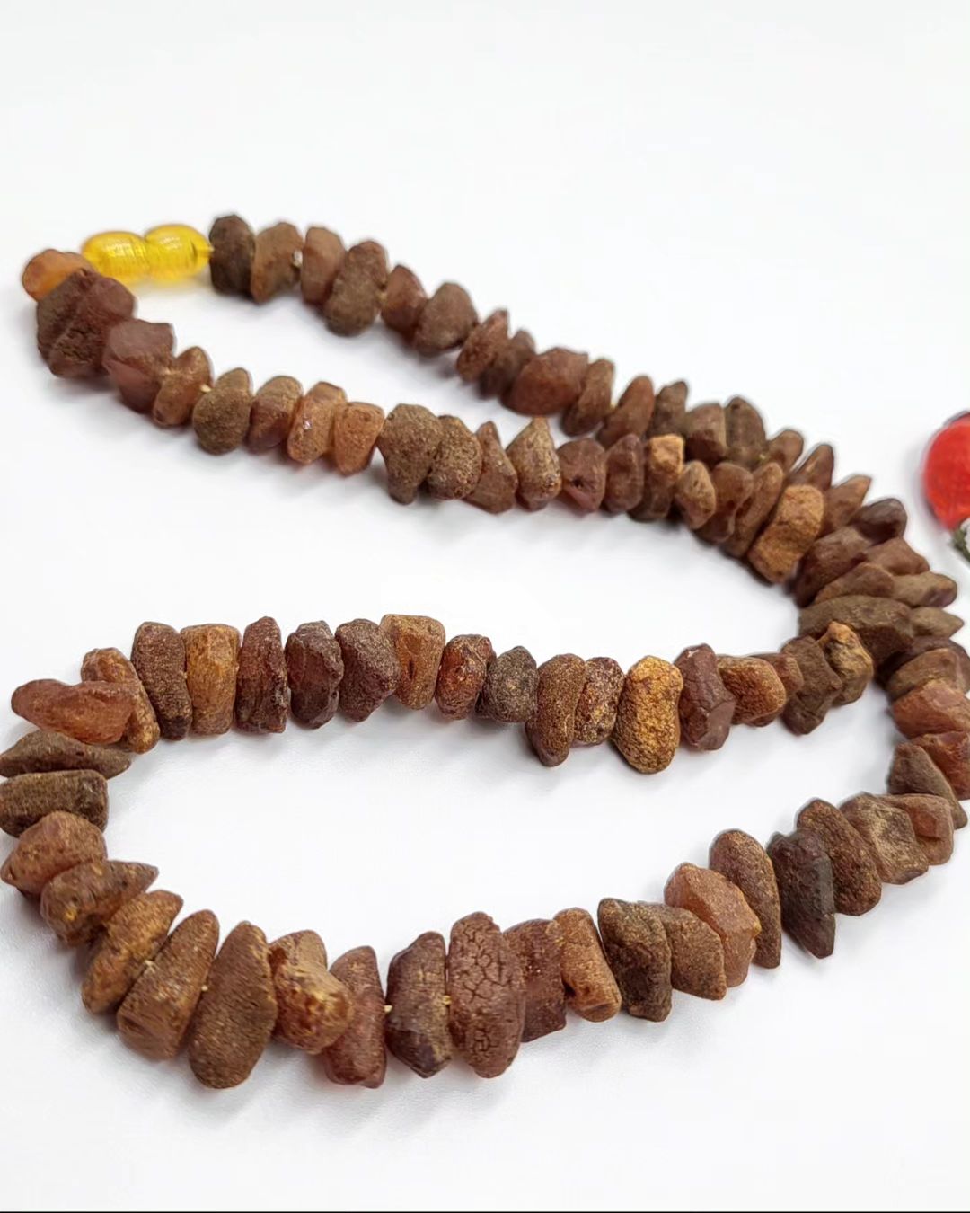 Nahaufnahme einer dunklen, unpolierten Bernsteinkette mit einzelnen rauen Steinen.

