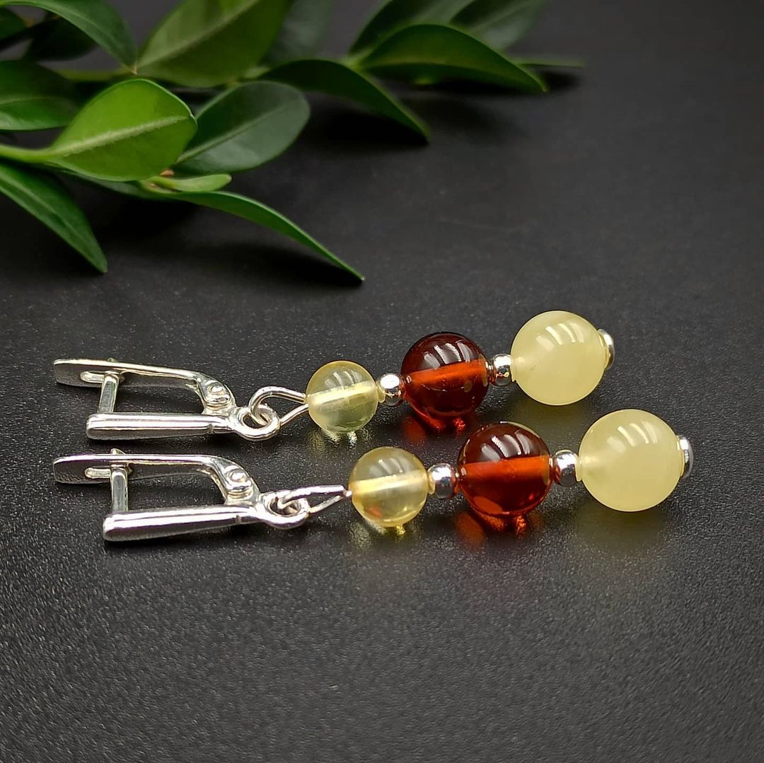 A pair of amber silver 3 beads earrings with sterling silver clasps, displayed on a dark background with a green leaf in the top right corner.