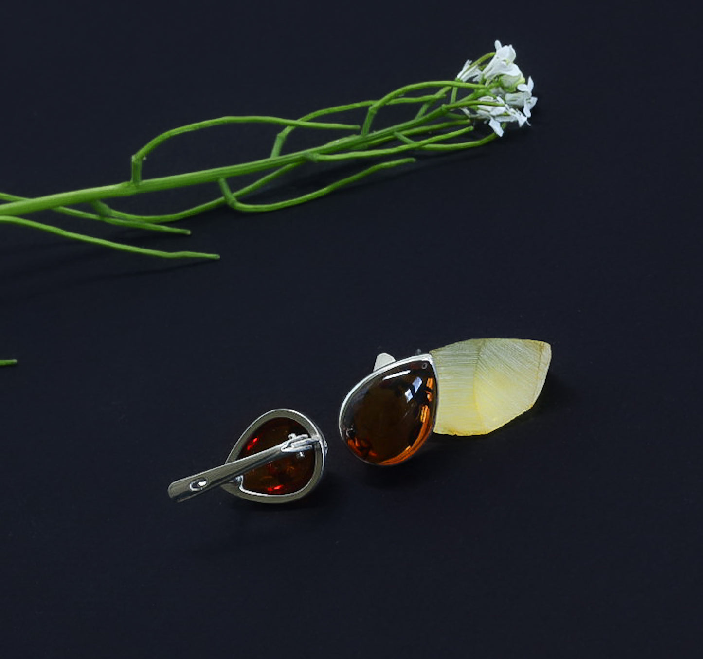 Two decorative brooches on a dark background with green leaves and white flowers.