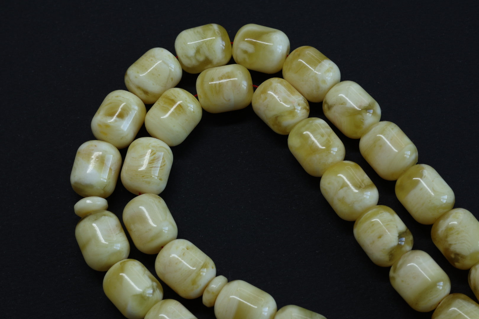 acro shot of the 10x8mm barrel-shaped amber beads from the Tetibel Tasbih, highlighting the natural marbling and smooth polish on a dark background.