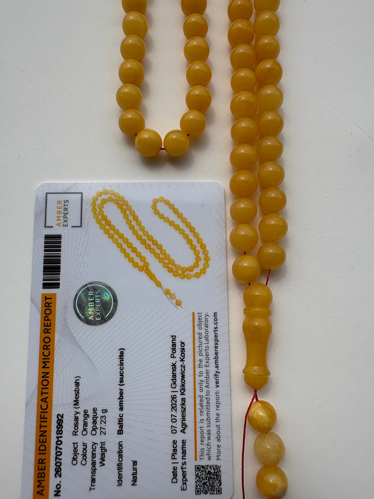 A strand of round yellow amber beads laid out next to an amber identification micro report card on a white background.