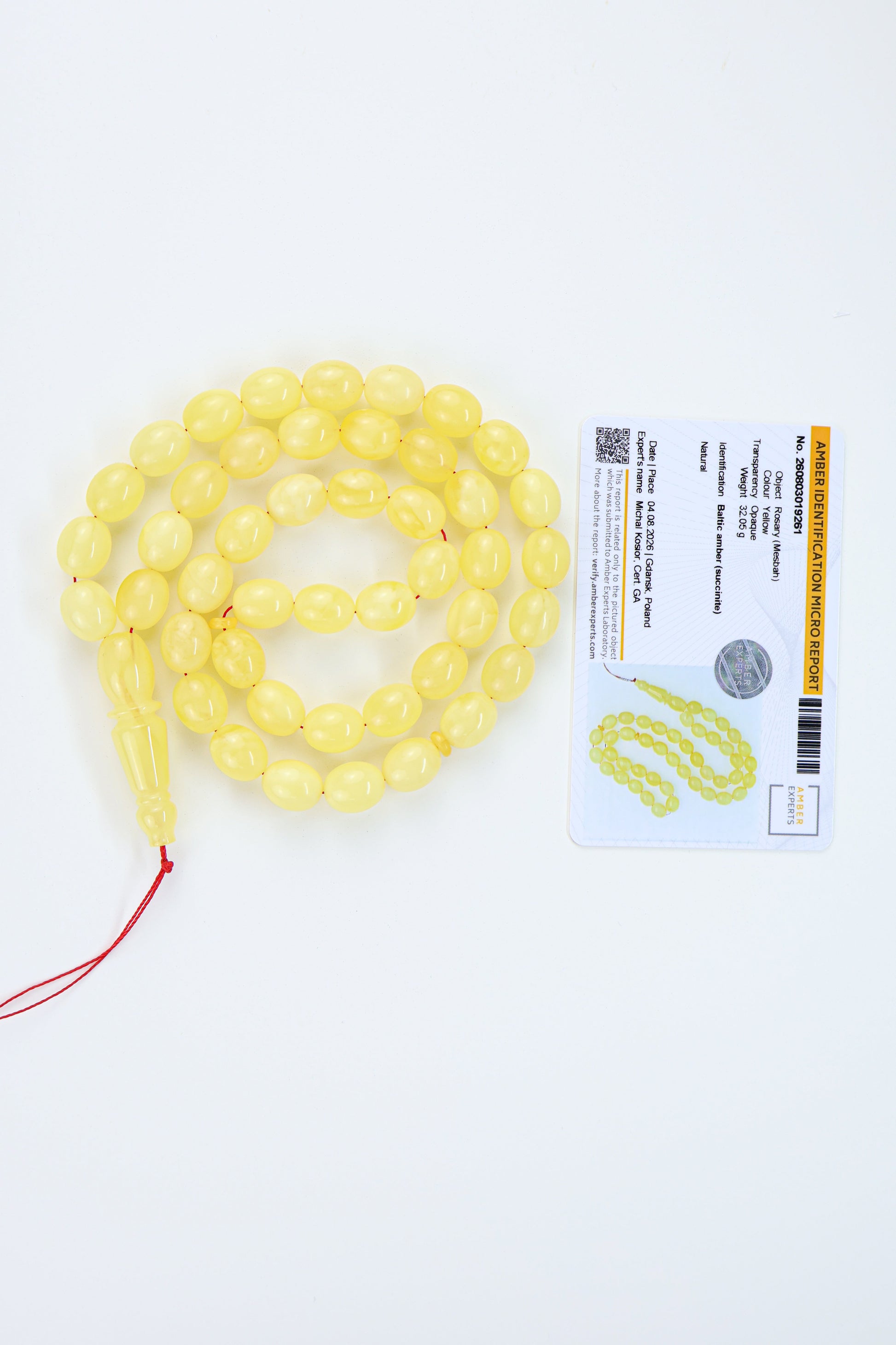Yellow amber  translucent prayer beads with a red cord and tassel, displayed next to a labolatory certificate card on a white background.