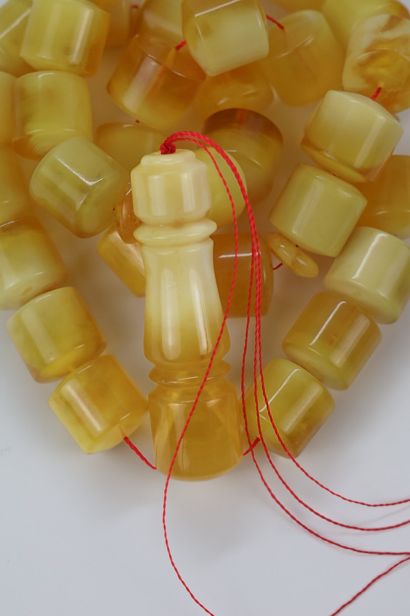 Detail of red thread drill hole in polished pressed Baltic amber rosary beads