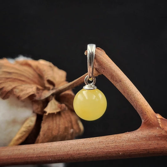 Nahaufnahme des glänzenden milchigen Bernstein Kugel Anhängers mit Silberfassung.