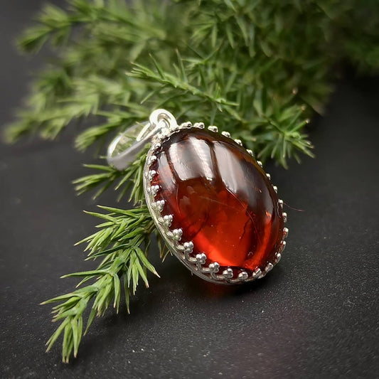 Vorderansicht des Tetibel dunkelkirschroten ovalen Bernstein Anhängers in 925er Sterling Silberfassung.