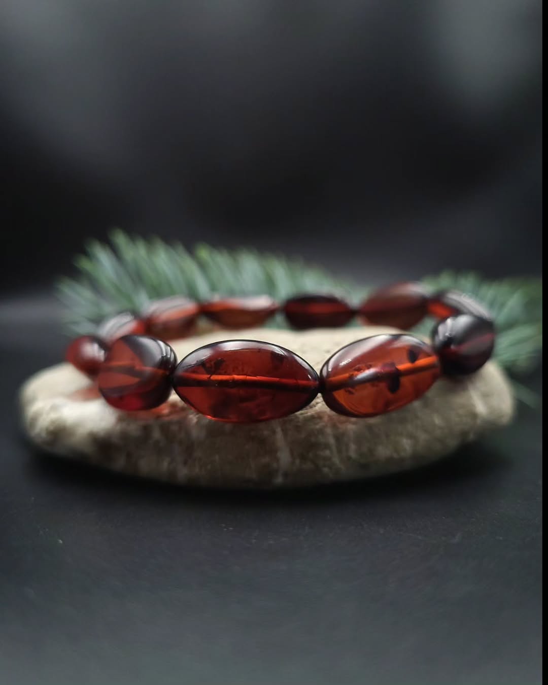 Echter Baltischer Bernstein in tiefroten Farben, polierte Olivenperlen auf dunklem Untergrund.