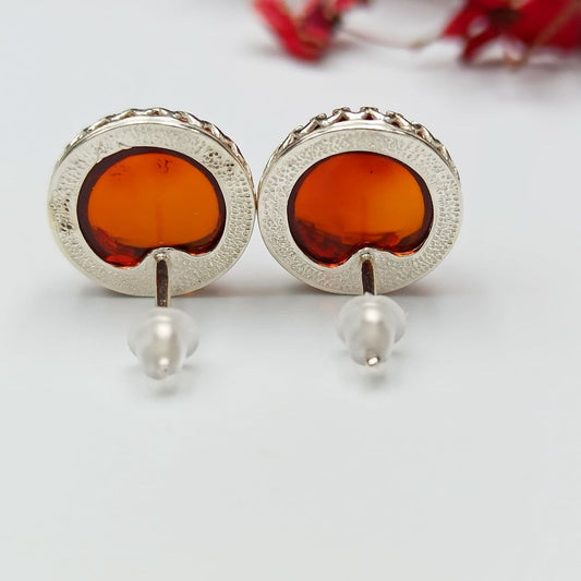 Handgefertigte Bernstein Ohrstecker von Tetibel Jewels auf schwarzem Hintergrund. Die Stecker bestehen aus ⌀12mm Cognac Bernstein und 925 Sterling Silber.