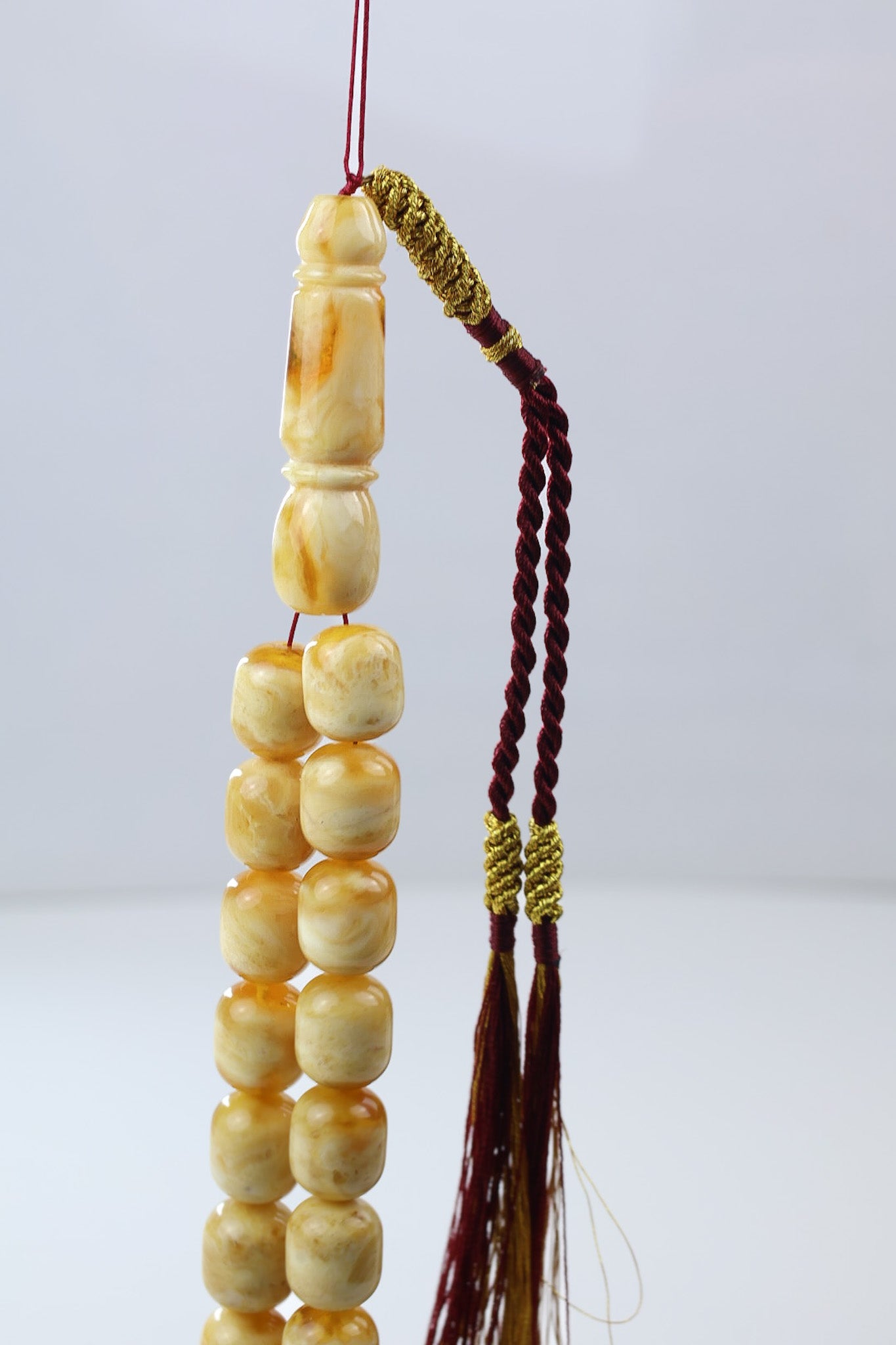 Close-up of cream and honey Baltic amber misbaha with carved imam bead and gold wrapped maroon tassel
