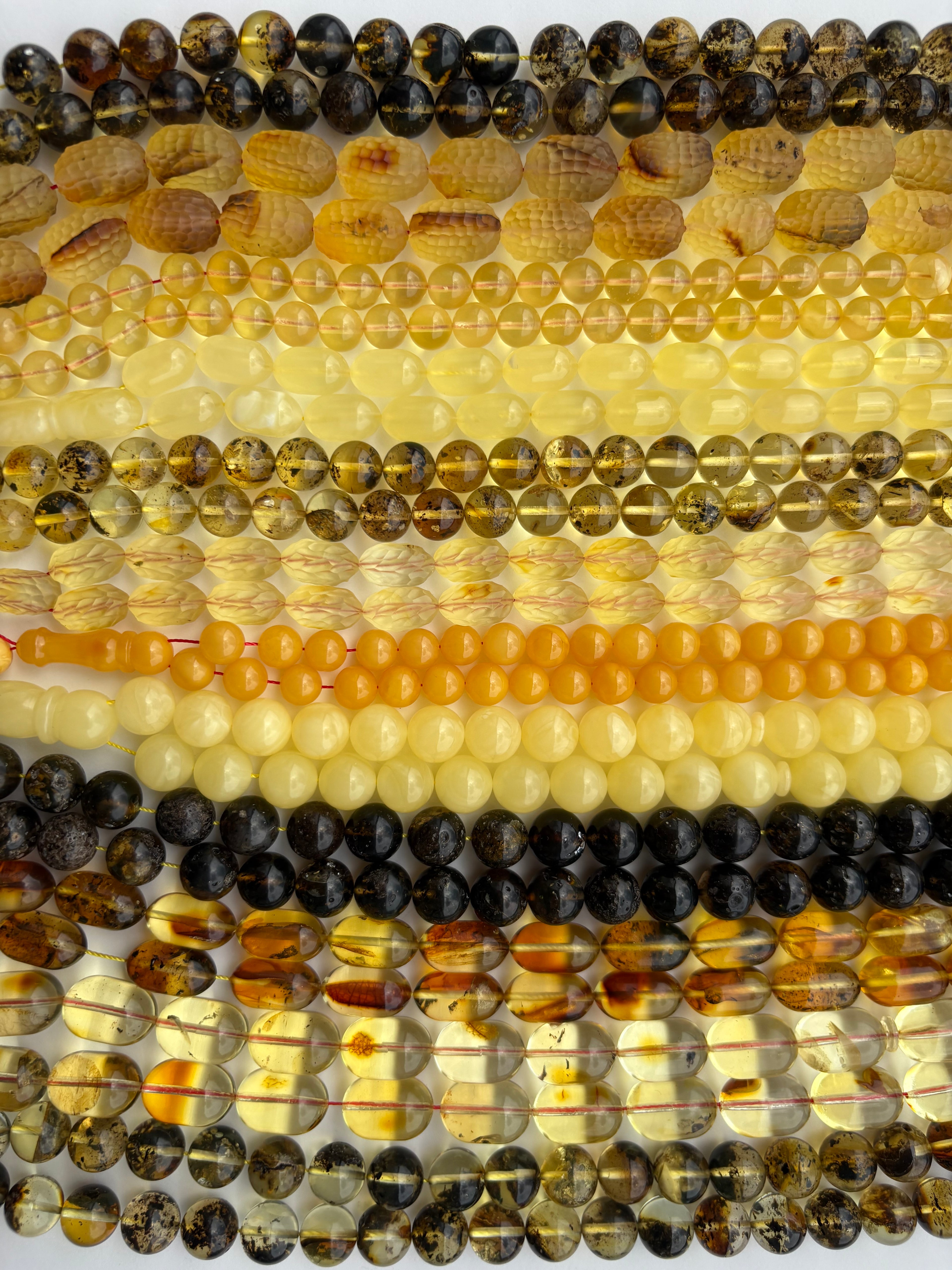 Multiple strands of polished natural amber beads in various natural colors, including amber, brown, yellow, cream, and black, arranged vertically.