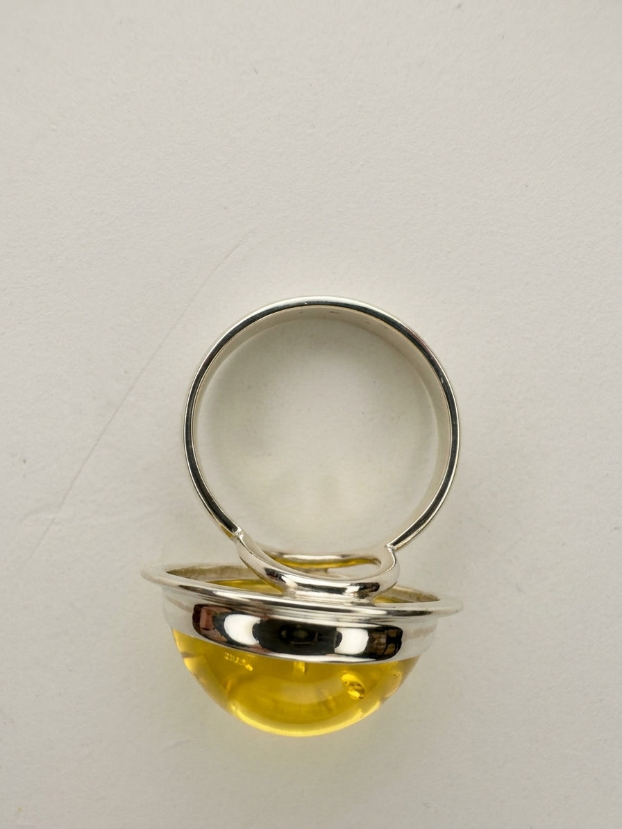 Side profile view of a handmade silver ring showcasing an elevated natural amber cabochon with openwork detail.