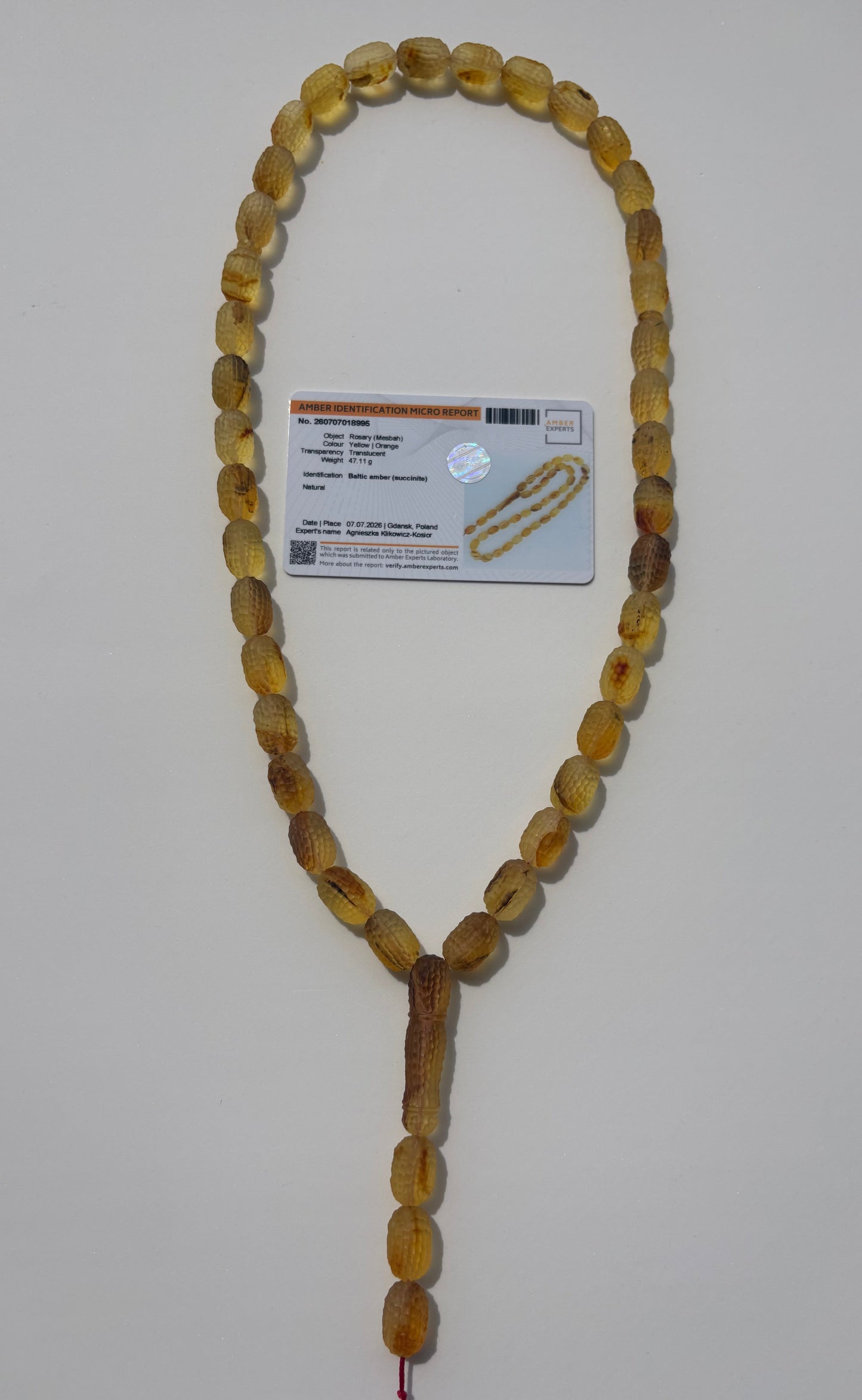 A strand of oval amber prayer beads with a tassel, laid out on a light gray background next to a product card.
