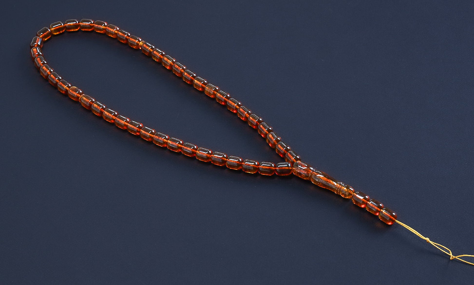Full view of the 30 g amber prayer beads (Bernstein Gebetskette), transparent brown on a dark background.