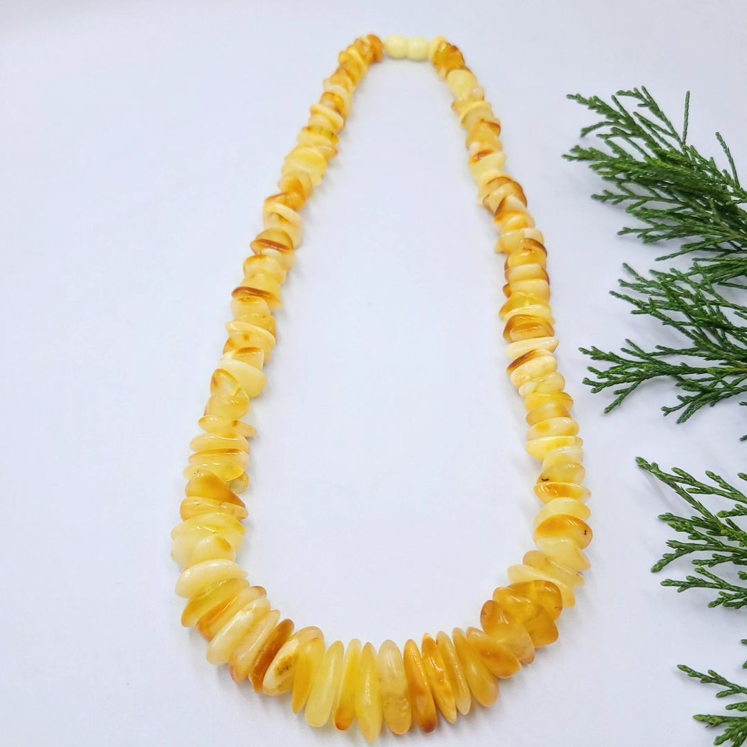 Tetibel Splitterkette aus echtem baltischem Rohbernstein in Butterscotch und Lemon, in Zick-Zack-Form auf weißem Hintergrund mit frischem Grün. Zeigt die ganze Länge und die unpolierten Nugget-Perlen.