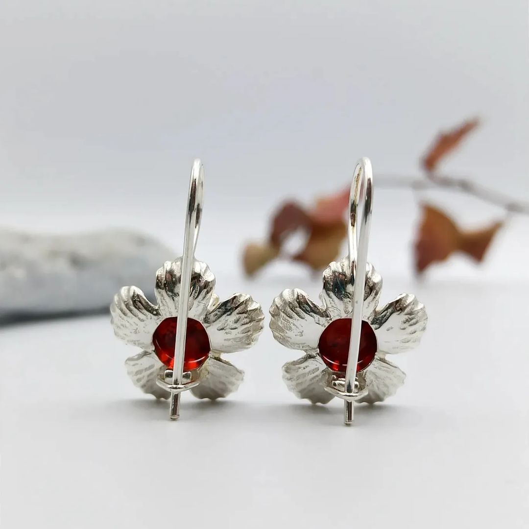 Silberne Ohrhänger mit Blütenform von Tetibel Jewels, zentriert mit Kirschbernstein. Detailansicht der hängenden Ohrringe.