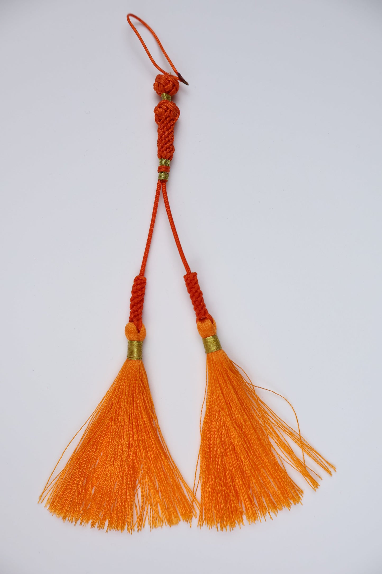 A traditional Islam orange silk tassel with braided red cords, gold spacer beads, and a small hanging loop, displayed on a clean white background.