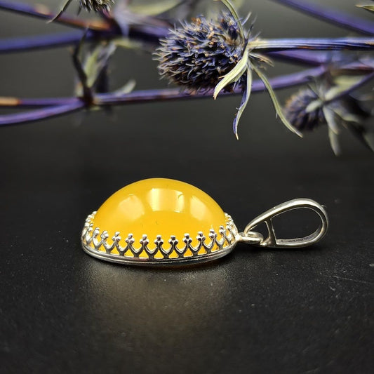 Seitenansicht des gewölbten Butterscotch Bernstein Anhängers mit dekorativer 925er Silberfassung.