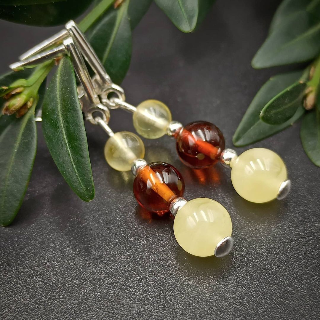 Winkelansicht der Tetibel Jewels Tricolor Baltische Bernstein Ohrhänger aus 925 Sterling Silber. Detailaufnahme der polierten Bernstein Perlen in Butterscotch, Cognac und Lemon Farben (⌀6-8mm) mit dem reflektierenden Silberverschluss und grünen Blättern.