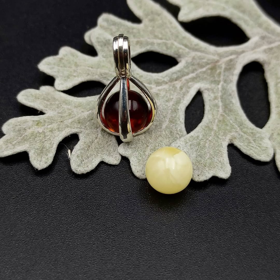 Silver pendant with red and yellow gemstones on a leafy background